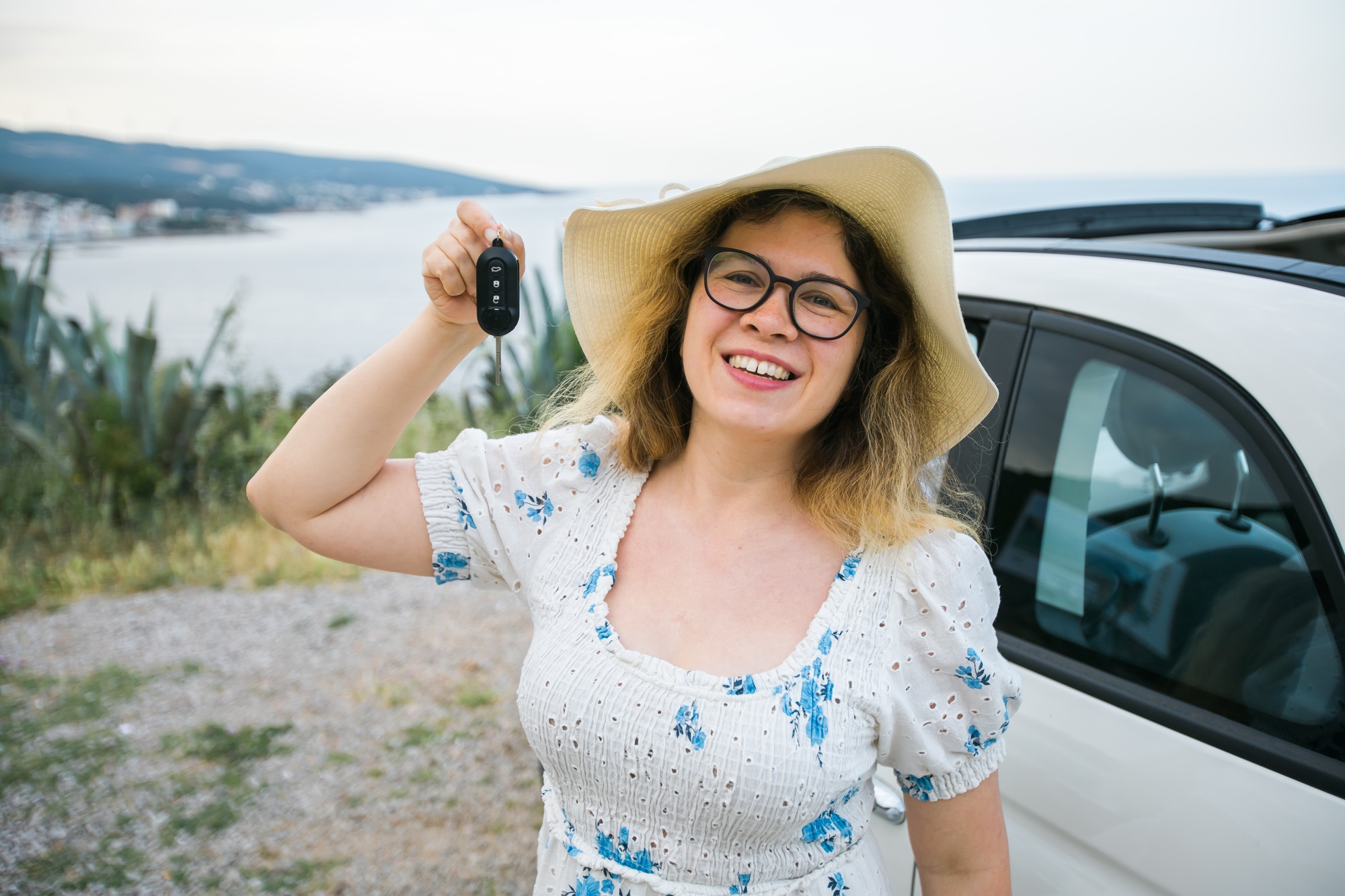 Car driver woman smiling showing new car keys and car. Female driving rented cabrio on summer